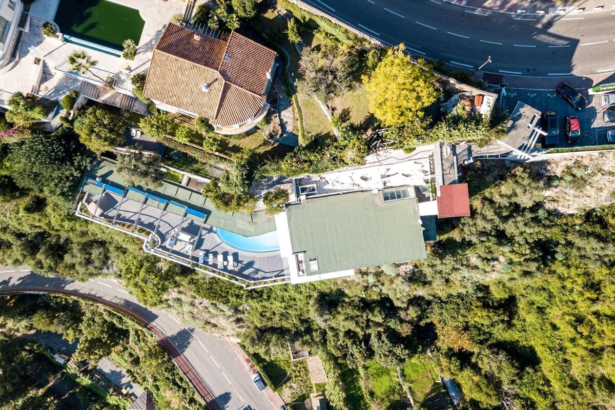 Aerial shot of houses, multiple pools, and winding roads set amidst lush green hills under clear skies.