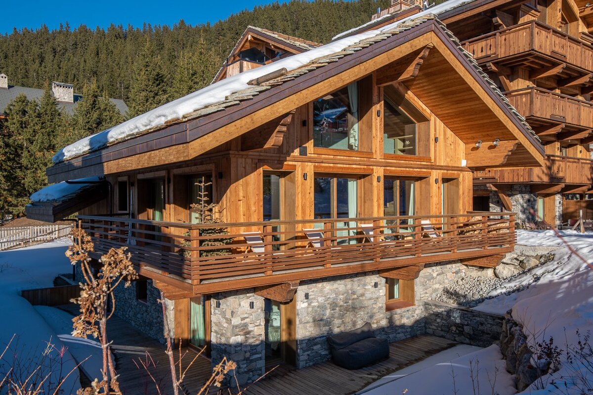 A cozy wooden and stone alpine chalet with a snowy roof, nestled in a winter forest landscape.