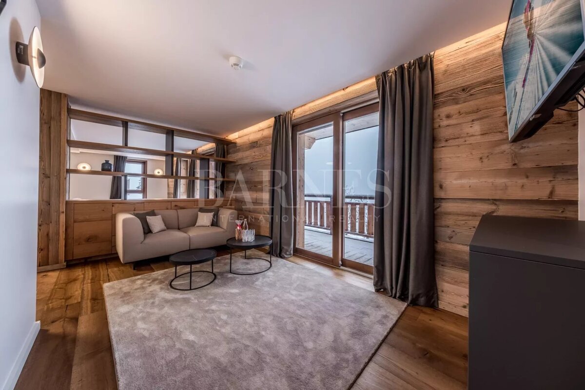 Modern chalet living room featuring rustic wood walls, a plush beige sofa, a large rug, and sliding doors opening to a balcony.