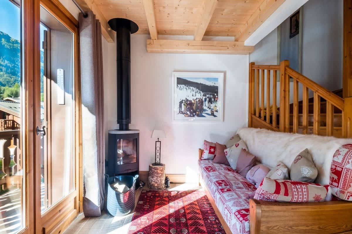 Cozy alpine chalet interior featuring a wood-burning fireplace, rustic wooden details, and a red patterned sofa.