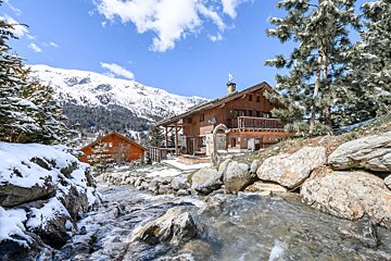 A house in the mountains with a stream running in front of it