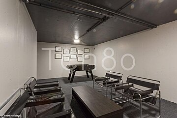 Modern game room featuring black leather chairs, a wooden coffee table, and a foosball table under a dark ceiling.