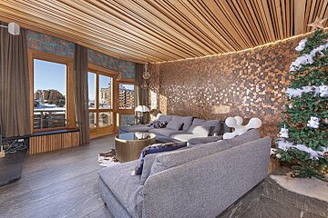 Modern living room with wood ceiling, copper tile wall, grey sectional sofa, and a decorated Christmas tree.