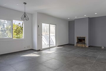 Spacious, empty room with white walls, grey tiled floor, large window, sliding door, a fireplace built into a grey wall, and modern lighting.