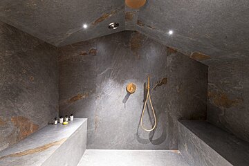 A bathroom with a stone wall and a gold shower head