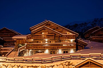 A large wooden house is lit up at night in the snow