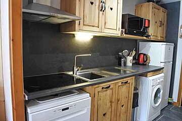 A small, rustic kitchen featuring light wooden cabinets with heart cutouts, a dark gray backsplash, and compact appliances.