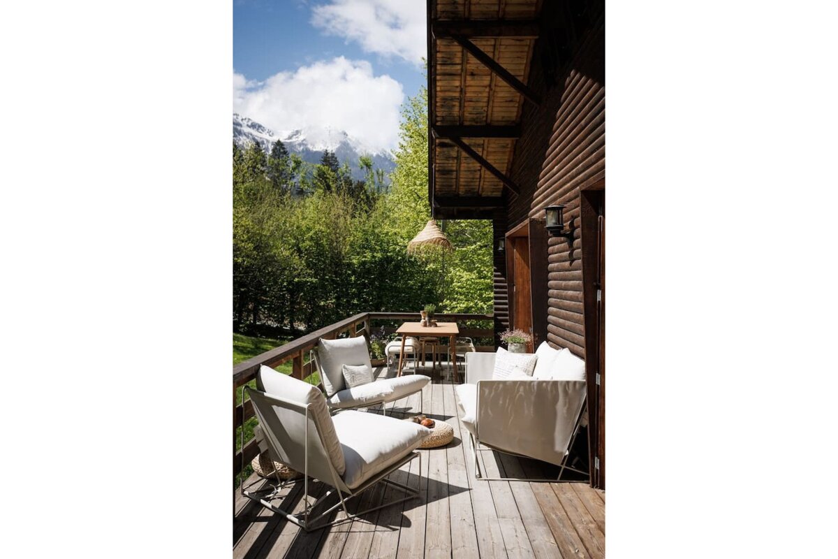 A wooden deck with chairs and a table with mountains in the background