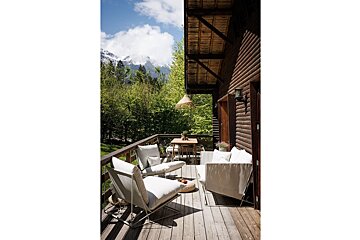 A wooden deck with chairs and a table with mountains in the background