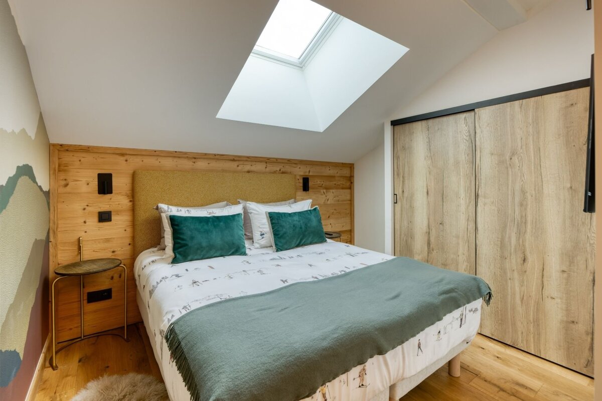 Cozy attic bedroom with a skylight, wooden headboard, ski-themed bedding, and green accents. Features a slanted ceiling and sliding closet doors.