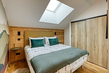 Cozy attic bedroom with a skylight, wooden headboard, ski-themed bedding, and green accents. Features a slanted ceiling and sliding closet doors.