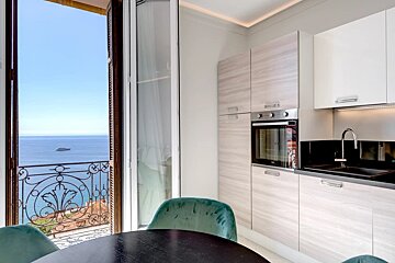 Modern kitchen and dining area opening onto a balcony with a stunning view of the blue ocean.