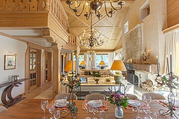 Luxurious alpine chalet interior with open-plan dining and living areas, wood paneling, chandeliers, and a grand fireplace.