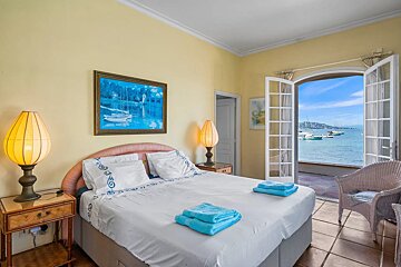 Bright bedroom featuring a double bed, yellow walls, and open French doors showcasing a scenic ocean view with boats.