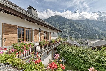 A house with a balcony filled with flowers and a mountain in the background