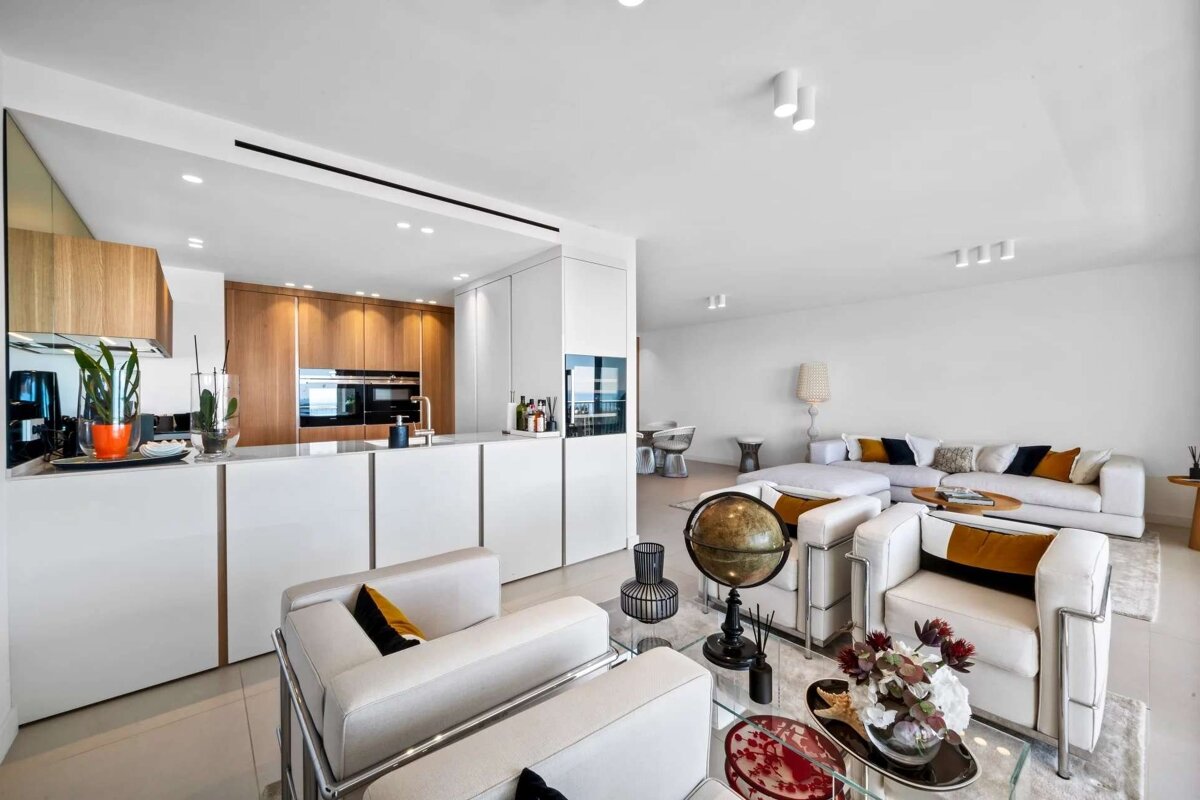 Modern open-plan kitchen and living room featuring white walls, wood cabinetry, and contemporary furniture, creating a bright and clean aesthetic.