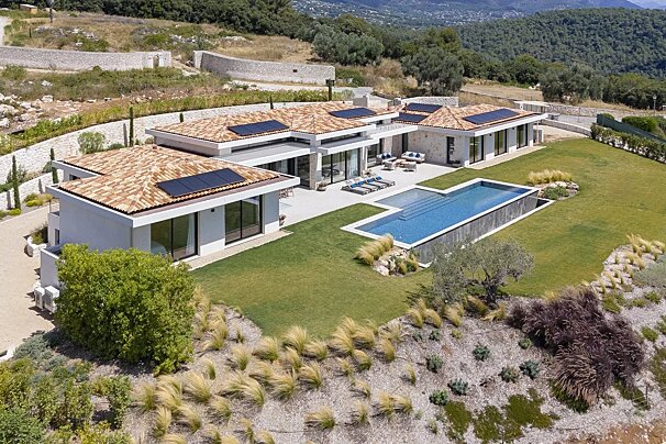 Aerial view of a luxury modern villa with a swimming pool, lawn, and solar panels, set in a scenic hillside landscape.