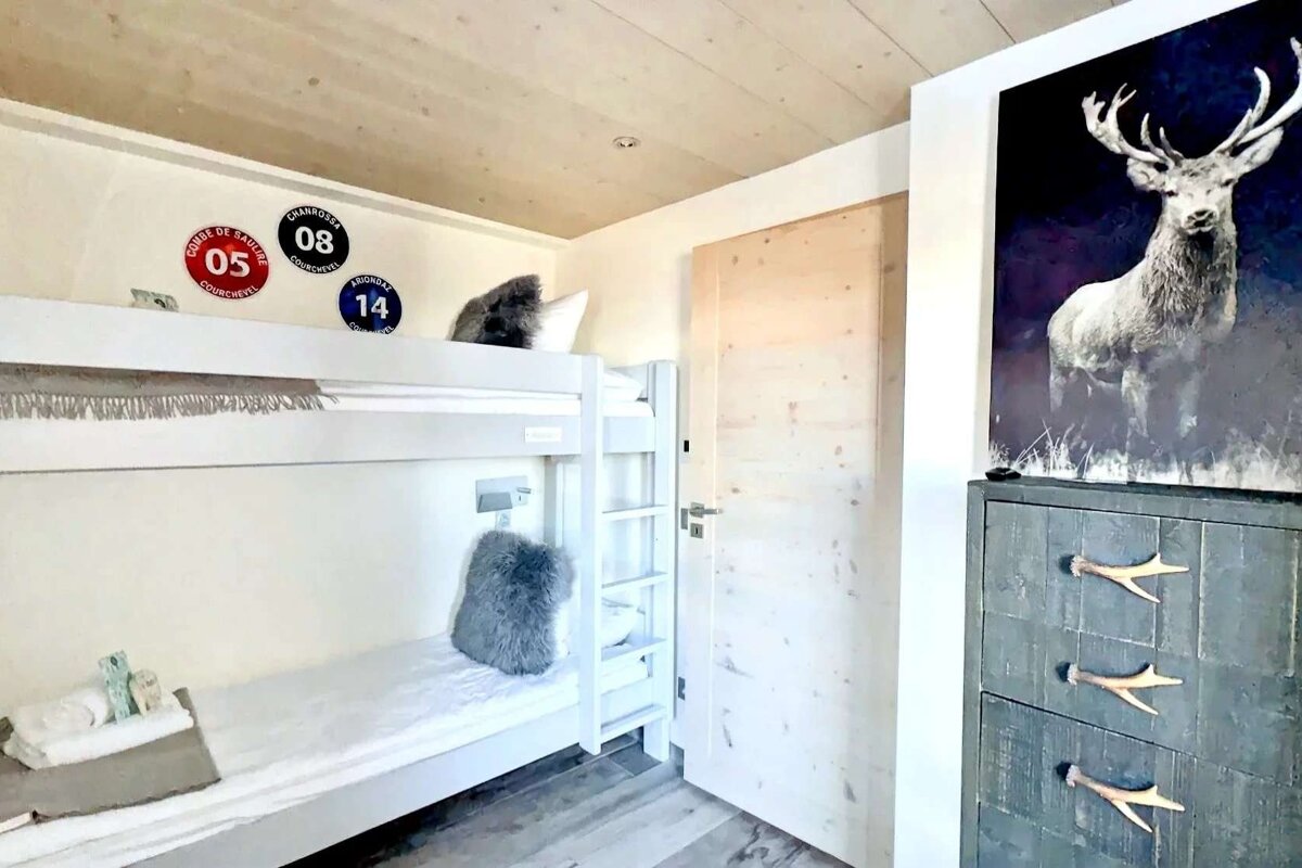 Cozy ski lodge bedroom with white bunk beds, Courchevel piste markers, a large deer print, and an antler-handled dresser.