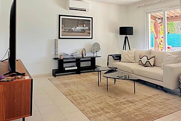 Modern living room with a white sofa, triangular coffee tables, a beige rug, and a framed vintage race car print on the wall.