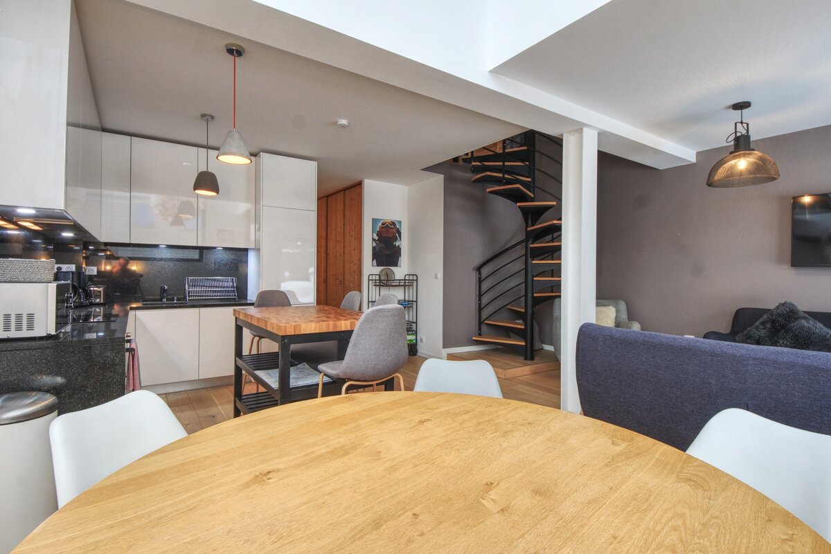 An open-plan living area features a modern kitchen, dining space, and living room with a prominent spiral staircase and contemporary decor.