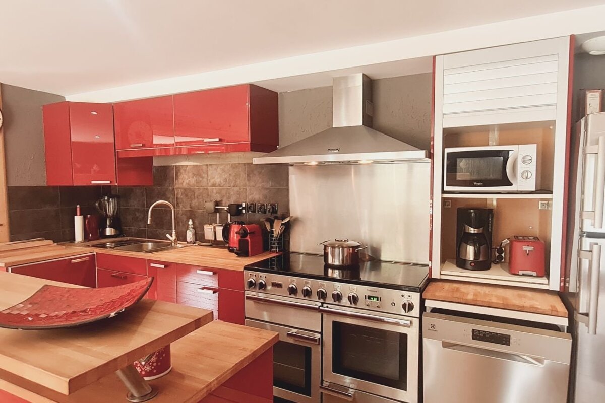 Modern kitchen featuring vibrant red cabinets, warm wooden countertops, and sleek stainless steel appliances.