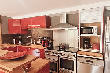 Modern kitchen featuring vibrant red cabinets, warm wooden countertops, and sleek stainless steel appliances.