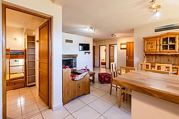 Cozy alpine apartment interior featuring wooden furniture, a fireplace, dining area, and a doorway leading to a bunk bed room.
