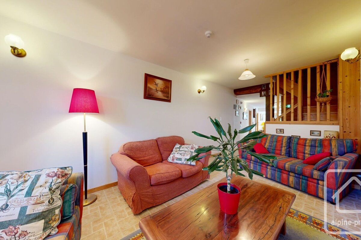 A cozy living room with a wooden coffee table, colorful sofas, potted plants, and warm lighting.