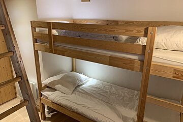 A simple wooden bunk bed neatly made with white sheets and pillows.