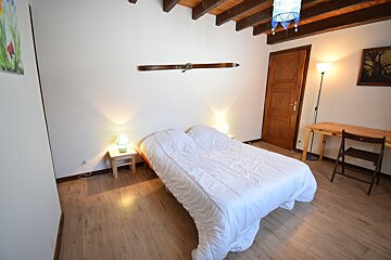 A cozy bedroom with a double bed, wooden floor, exposed beams, and white walls. Includes bedside tables, a desk, and a decorative ski.