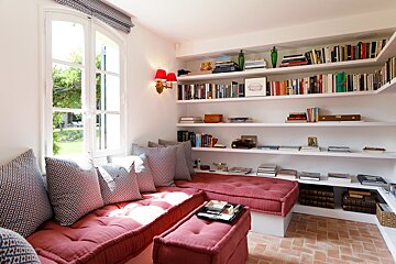 A corner of a room with bookshelves and a red ottoman
