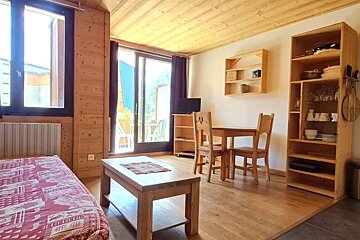Cozy wooden cabin apartment with a dining set, coffee table, shelving, and large glass door opening to a balcony.