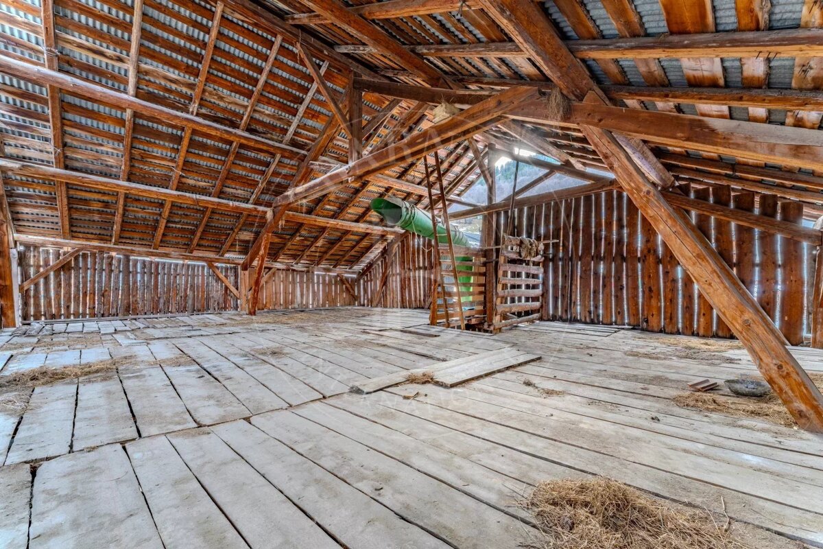 Inside of a wooden barn loft with exposed beams, plank floors, and a green chute leading down.