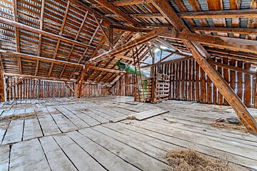 Inside of a wooden barn loft with exposed beams, plank floors, and a green chute leading down.