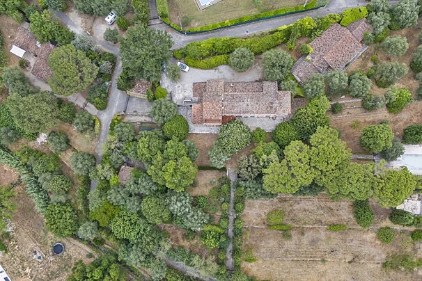 Aerial view of a sprawling property with red-roofed buildings, winding roads, lush green trees, and dry, open land.