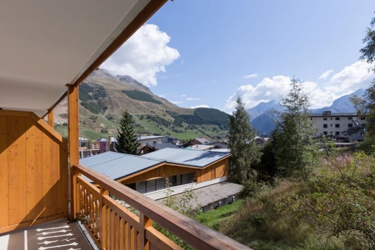 Scenic view of an alpine valley and village from a wooden balcony under a blue sky.