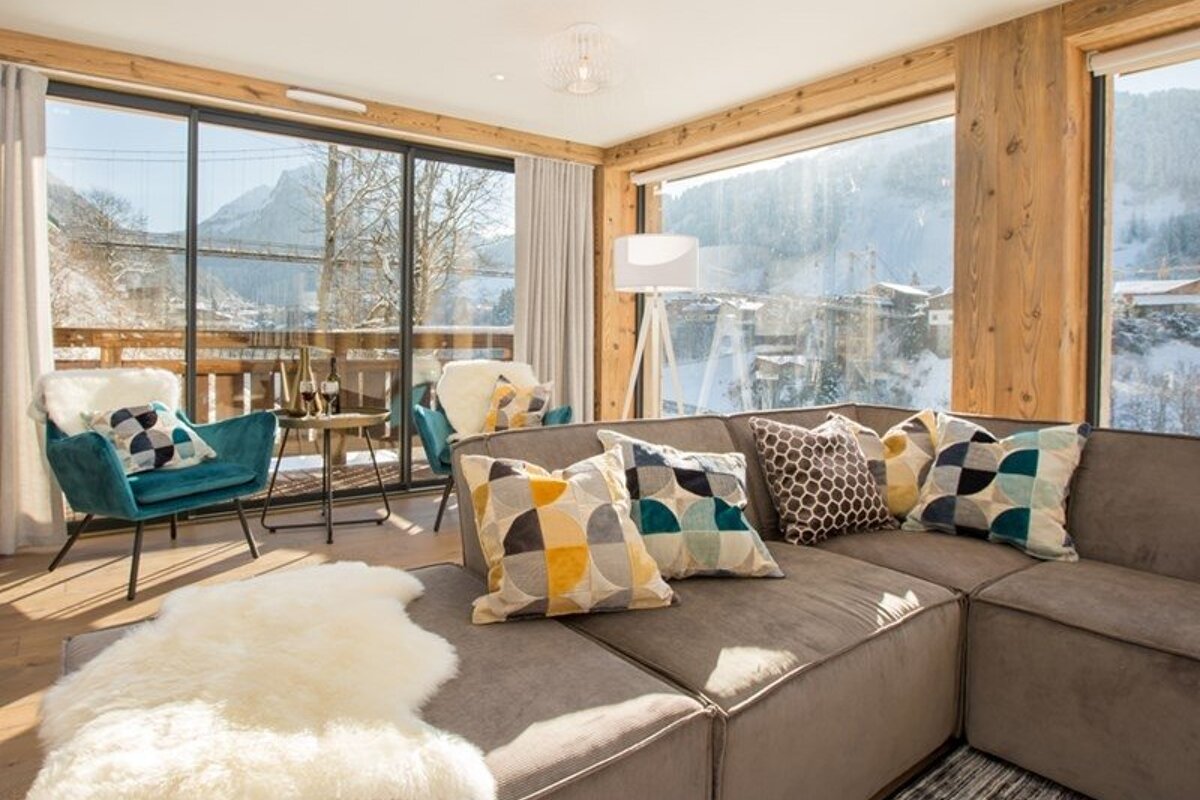 Cozy chalet living room featuring a brown sectional, colorful pillows, and large windows overlooking a snowy mountain landscape.