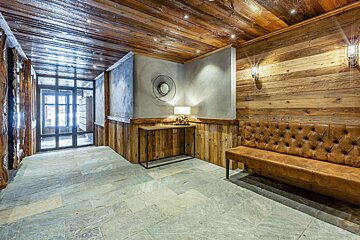 Rustic entryway with warm wood walls/ceiling, cool stone floor, leather bench, and modern chalet decor.