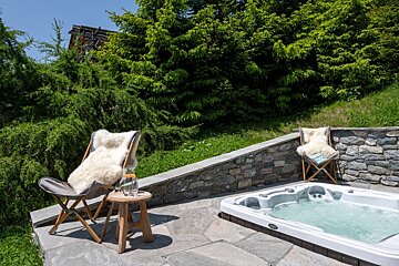 A hot tub is surrounded by chairs and a stone wall