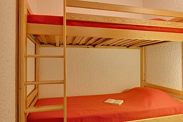 A bunk bed with red sheets and a book on it