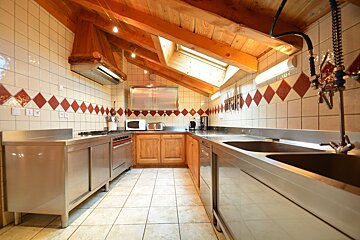 An attic kitchen featuring a wooden vaulted ceiling, skylight, stainless steel surfaces, and tiled walls with red diamond accents.