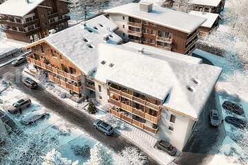 Aerial view of snow-covered modern chalets in a winter mountain village, with cars parked on roads and frosty trees.