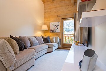 Cozy cabin living room featuring a beige sectional sofa, wood-paneled walls, a white TV console, and a door to a balcony.