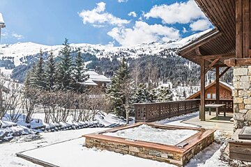 A hot tub on a snowy deck with mountains in the background