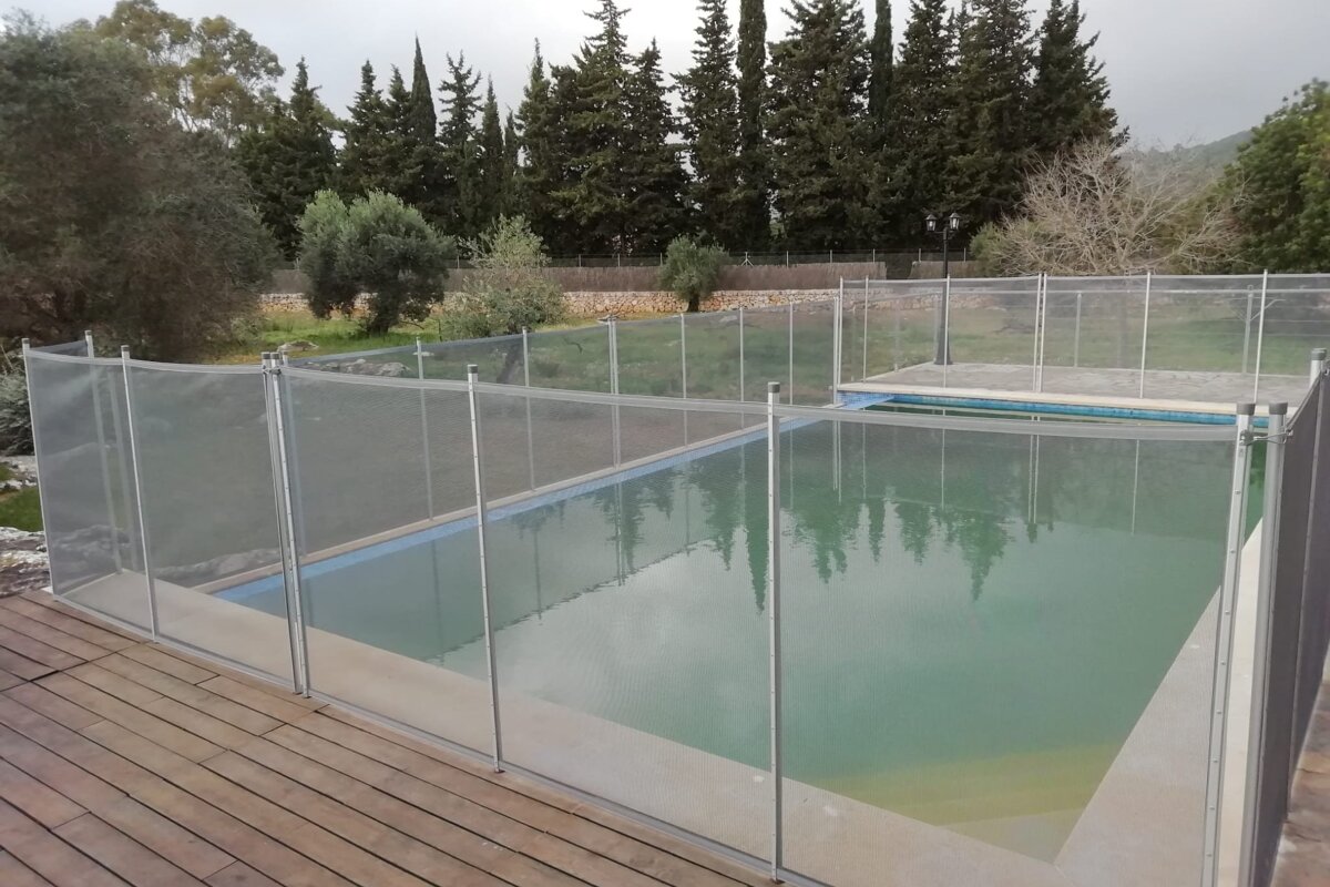 A fence surrounds a swimming pool with trees in the background