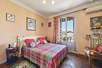 A colorful, vintage-style bedroom with peach walls, a plaid bedspread, wood floor, and balcony access to rooftops.