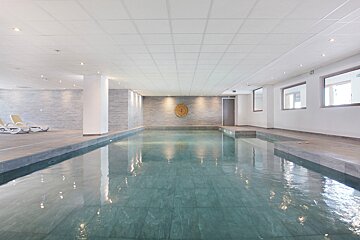 A large indoor swimming pool with a green exit sign on the wall