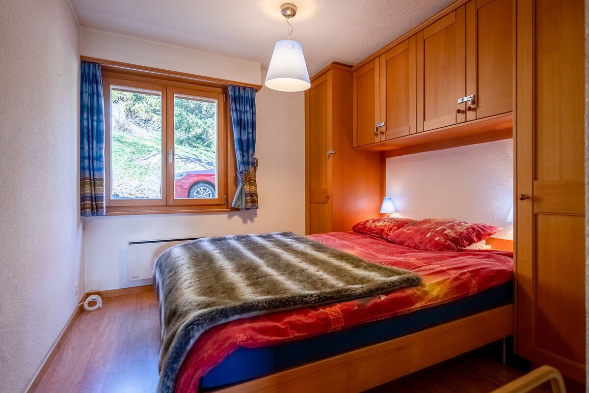 A bedroom with a bed and a window with a red car in the background