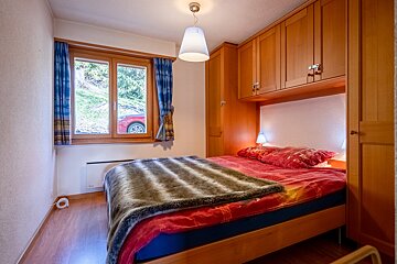 A bedroom with a bed and a window with a red car in the background