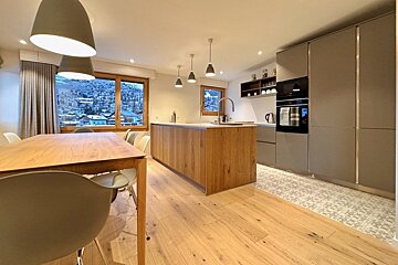 Modern open-plan kitchen and dining area with light wood accents, a large central island, grey cabinets, and a snowy mountain view.